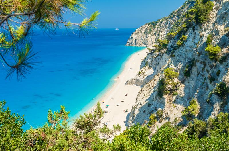 Aussicht auf einen langen weißen Strand und dem türkisen Meer mit Felsen und grüner Natur im Zakynthos Urlaub mit Kindern