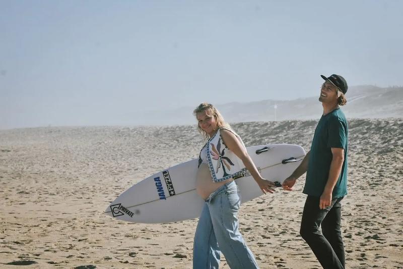 Schwangere Frau mit Surfbrett im Familienurlaub Surfen