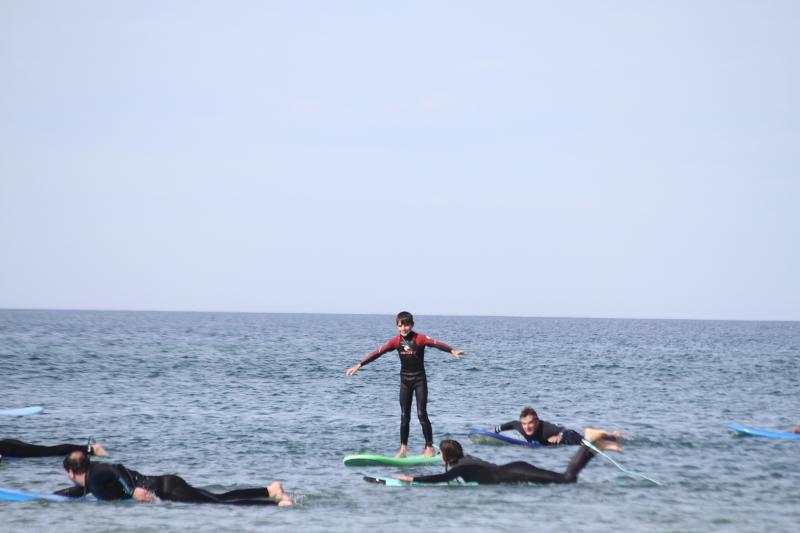 Kind surft mit Surfcoaches und lernt wie man steht im Wasser