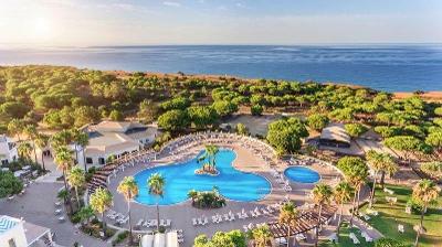 Poolanlage mit kleiner Palmeninsel und vielen Bäumen umgeben unweit vom Meer im Familienurlaub Portugal