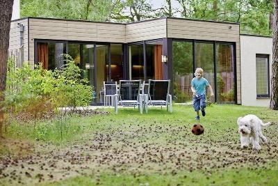 Kind und Hund spielen Ball vor einem modernen Ferienhaus im Familienurlaub Niederlande