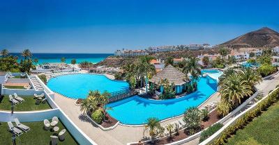Große Poolanlage mit vielen Palmen und Meer im Hintergrund im Familienurlaub Fuerteventura