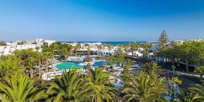 Pool versteckt hinter Palmen und Meer im Hintergrund im Familienurlaub Lanzarote