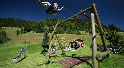 Kinder schaukeln auf dem Spielplatz in den Bergen im Familienurlaub Österreich