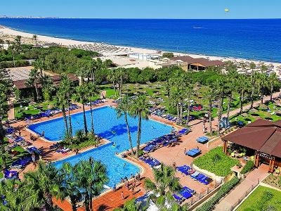Pool mit Sonnenliegen und Palmen und Weg zum Meer im Familienurlaub Tunesien