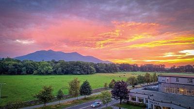 Grünes Feld mit einem Berg, im Hintergrund ist ein Sonnenuntergang
