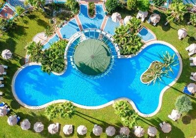 Wunderschöner Pool aus der Vogelperspektive. Umrandet von grünen Palmen und Sonnenschirmen