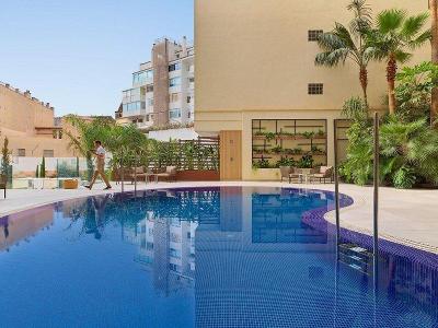 Dunkelblauer Pool mit Palmen vor gelbem Hotelgebäude im Familienurlaub Mallorca