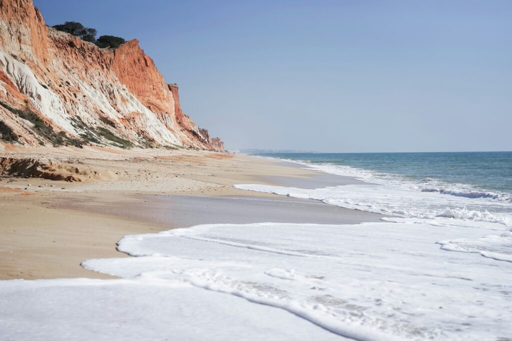 Tipps Familienurlaub: Algarve. Weiter Sandstrand am Meer mit orangenen Klippen.