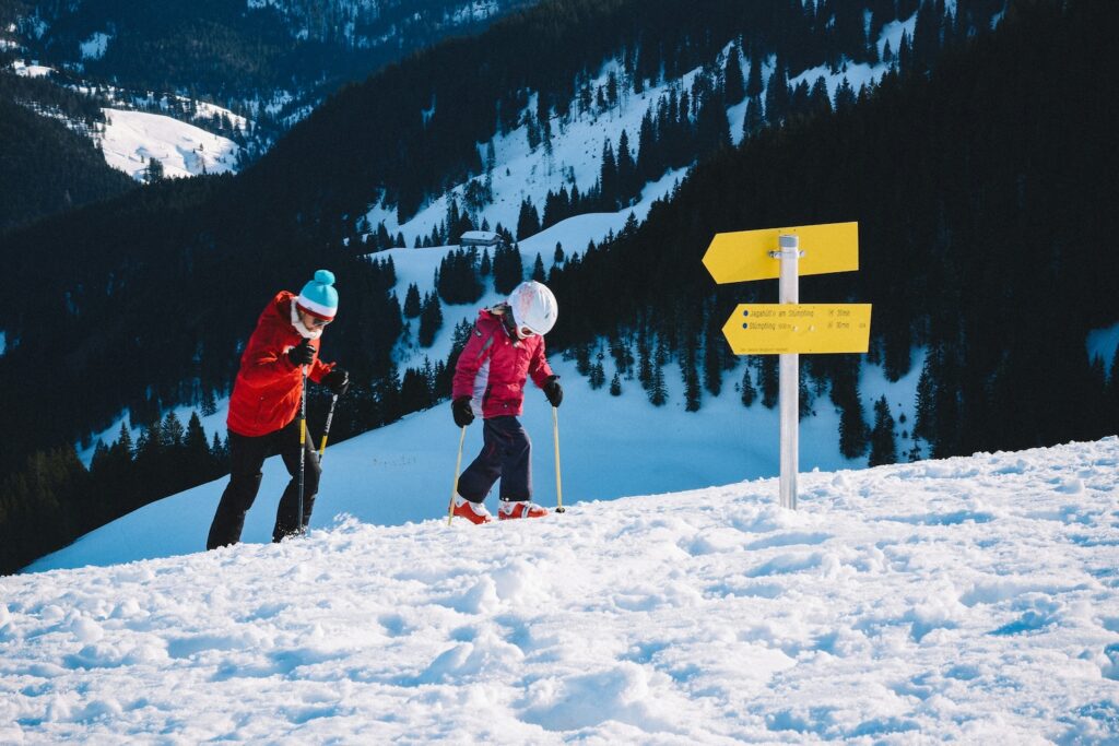 Wohin Urlaub mit Kindern? Menschen die in einer Schneelandschaft spazieren gehen. Rechts ist ein gelbes Schild mit Wegbeschreibungen. Im Hintergrund kann man Tannenlandschaften erkennen.