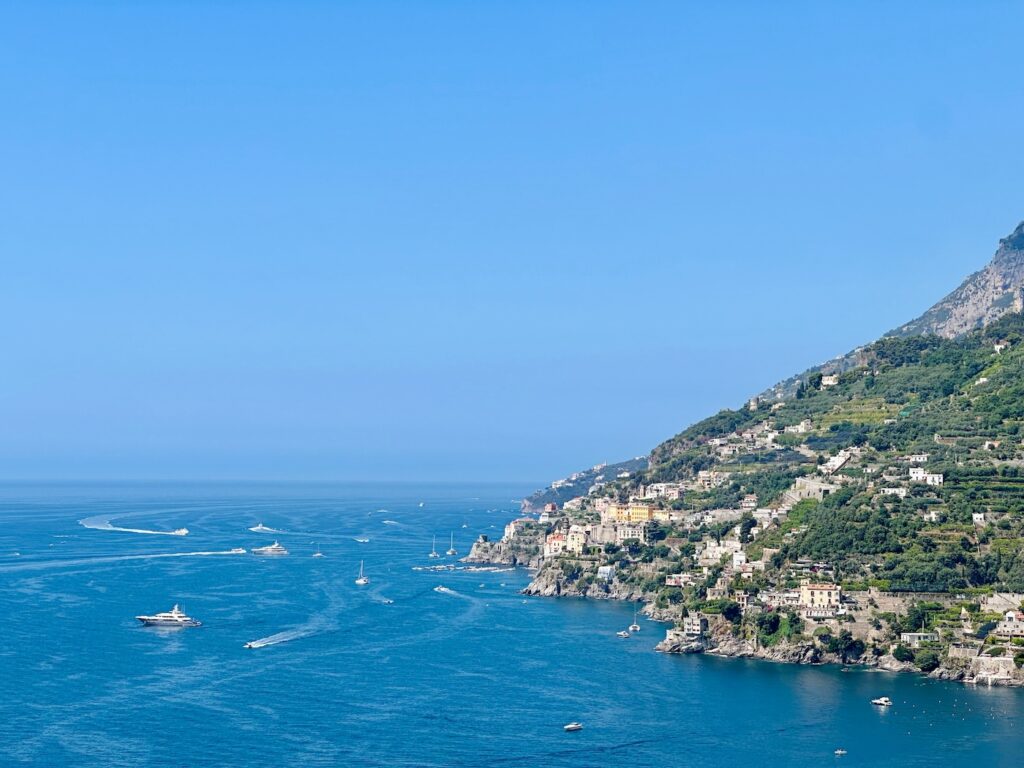 Wohin Urlaub mit Kindern? Ausblick auf die Amalfiküste mit Meer, Booten und die Küste, auf der Häuser zu erkennen sind bei schönem sonnigen Wetter.