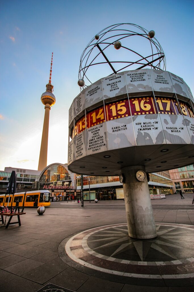 Der Alexanderplatz mit der Weltzeituhr im Vordergrund und dem Fernsehturm im Hintergrund bei blauen Himmel im Urlaub mit erwachsenen Kindern