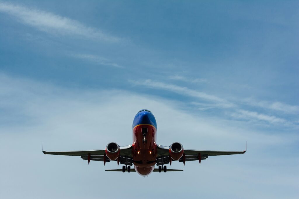 Tipps Familienurlaub: Flüge spannend gestalten. Ein fliegendes Flugzeug in rot und blau bei schönem Wetter.