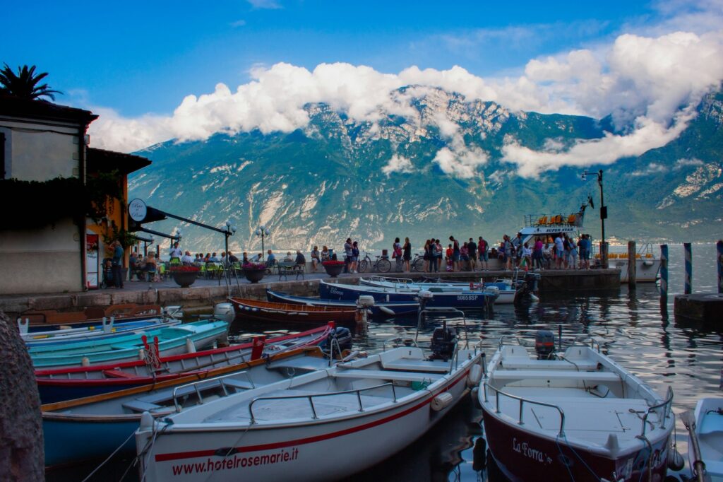 Tipps Familienurlaub: Gardasee. Mehrere Boote in einem kleinen Hafen am See mit einer Hauswand und den Bergen im Hintergrund.