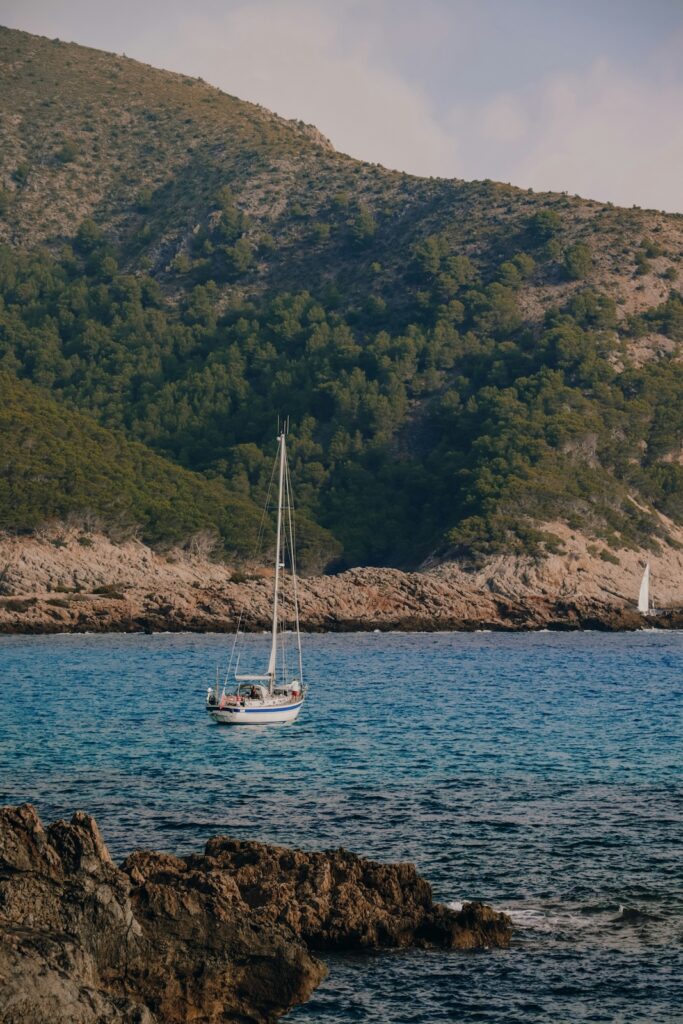 Familienurlaub Tipp: Mallorca. Eine Bucht am Meer mit Bergen im Hintergrund. Auf dem Meer sieht man ein kleines Segelboot.