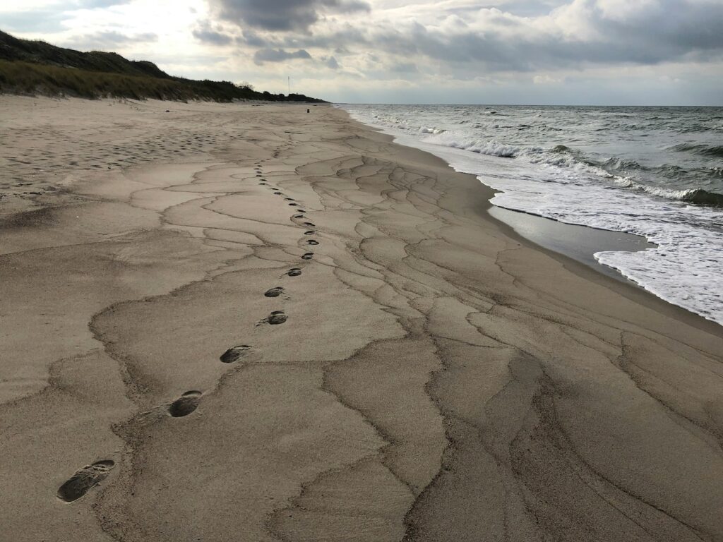 Familienurlaub Tipps: Sandstrand im Familienurlaub Deutschland mit Fußspuren und dem Meer bei wolkigen Wetter