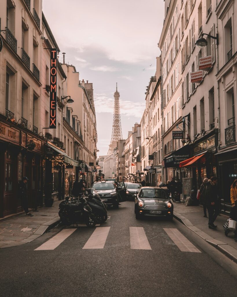 abenteuerlicher Herbstferien Urlaub mit Kindern wohin? Eine Straße in Paris mit Zebrastreifen und Autos, im Hintergrund der Eiffelturm 