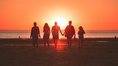 Alles rund um Tipps Familienurlaub. Eine Familie am Strand. Im Hintergrund sieht man das Meer und den Sonnenuntergang.