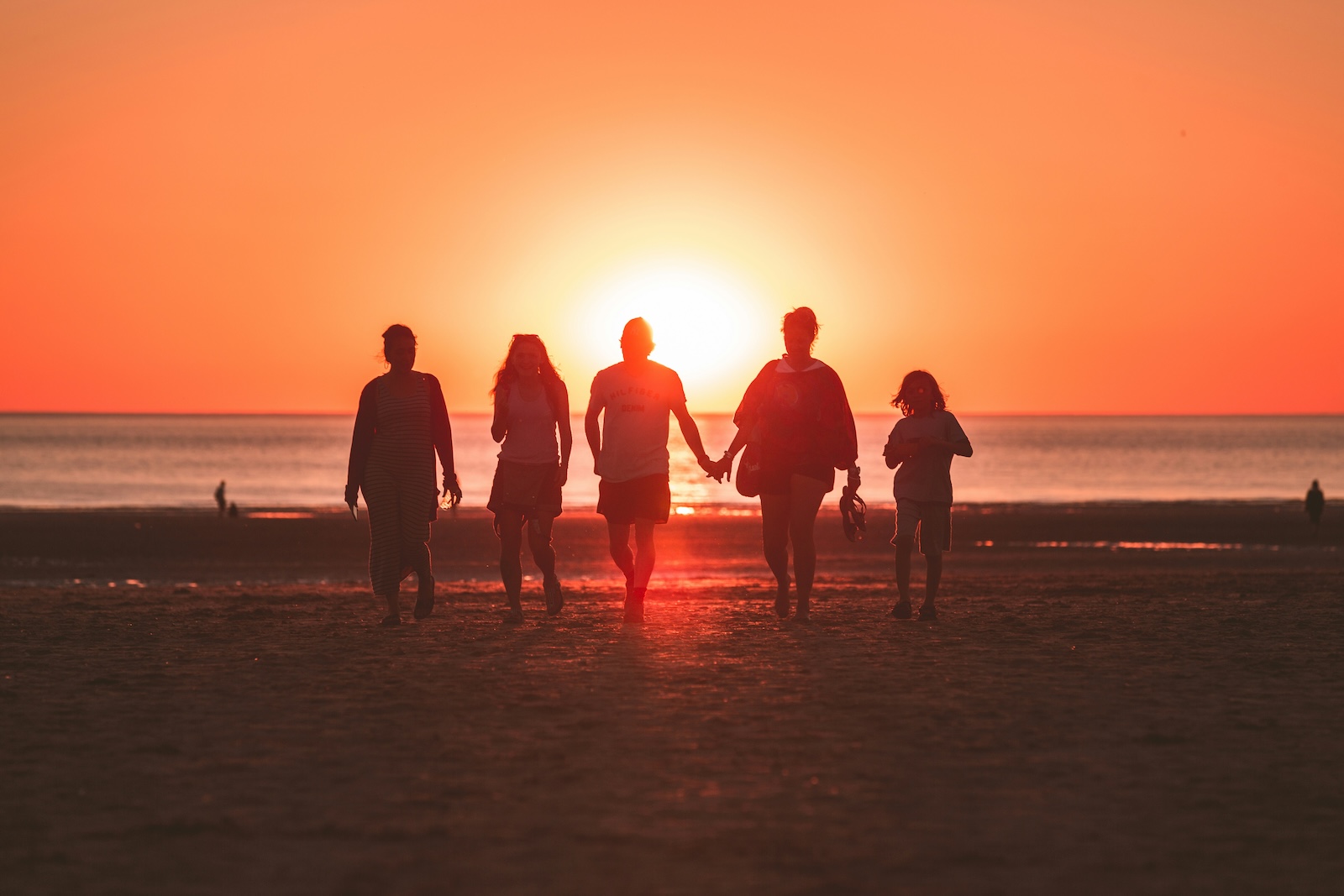 Alles rund um Tipps Familienurlaub. Eine Familie am Strand. Im Hintergrund sieht man das Meer und den Sonnenuntergang.