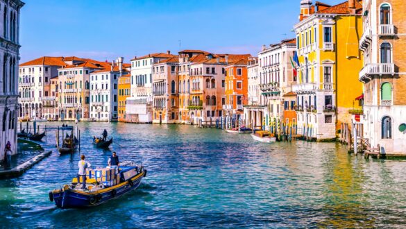 ein Kanal in Venedig mit bunten Häusern und blauen Wasser. Auf dem kanal befinden sich Gondulafahrer und Boote im Kurzurlaub mit Kindern