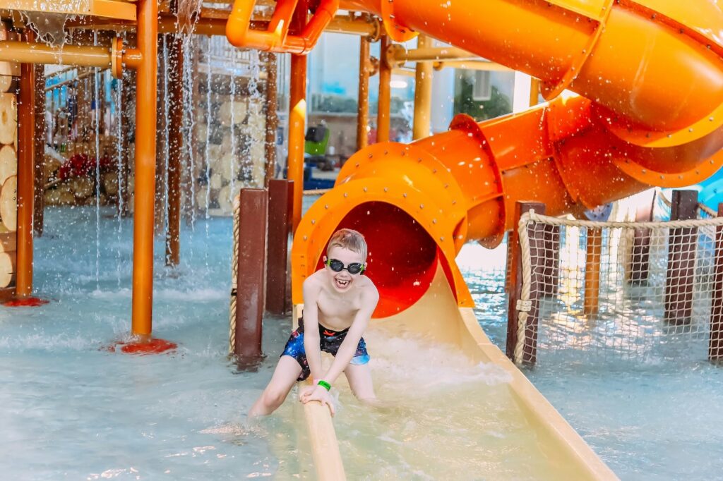 Wohin in den Urlaub mit Kindern? Eine orangene Wasserrutsche in einer Poolanlage auf der ein Kind rutscht.